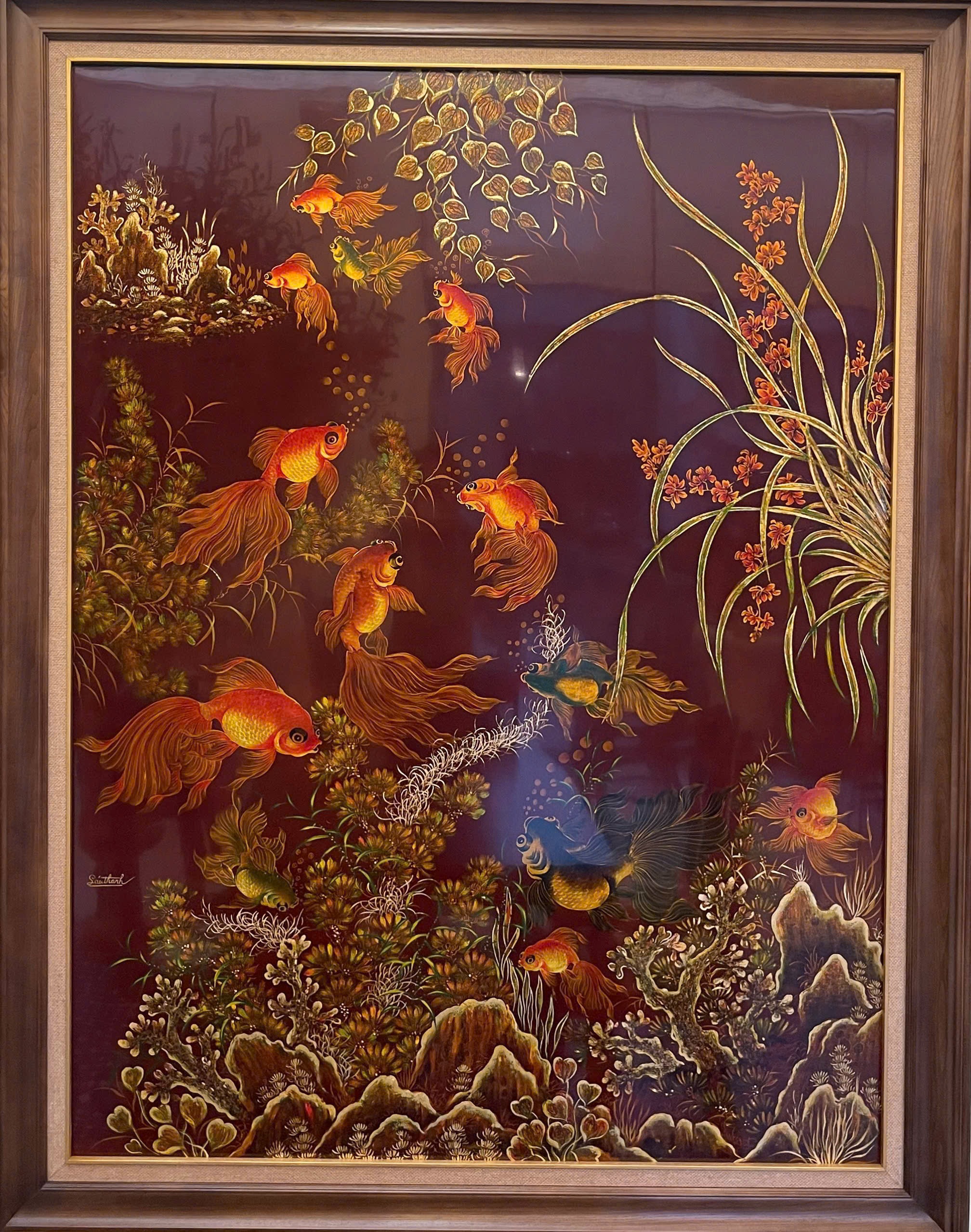 Ngư tảo — Goldfish weave between orchids, rock forms and aquatic plants in a tall red-brown composition. Flowing tails and fine gold-toned linework carry the eye through the work.